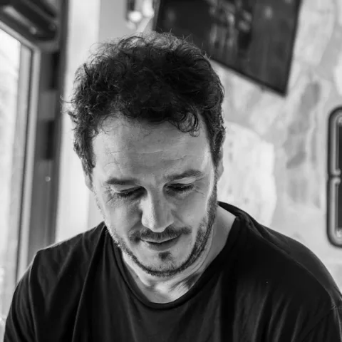Retrato en blanco y negro de Esteban de Aymerich, con la mirada baja, camiseta oscura y una pared de piedra al fondo