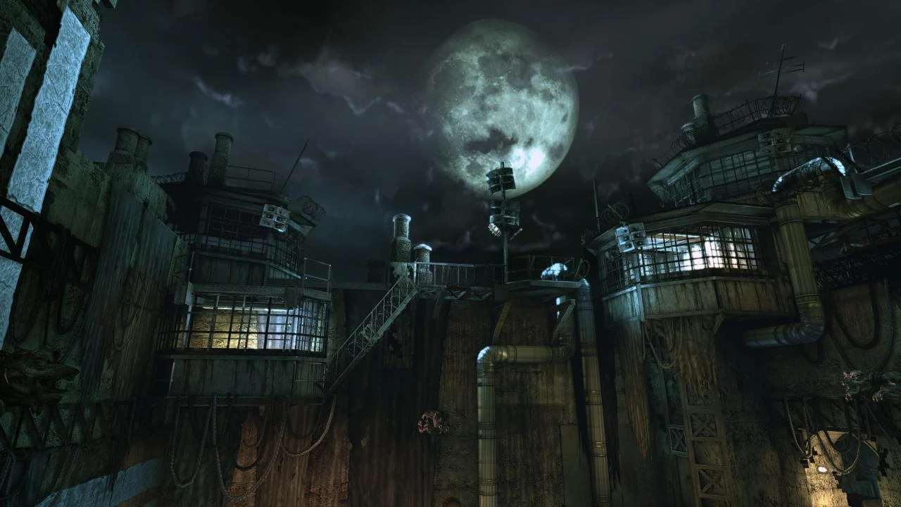 Los edificios del Asilo Arkham de noche, con pasarelas metálicas, tuberías y ventanas iluminadas bajo una luna llena entre nubes