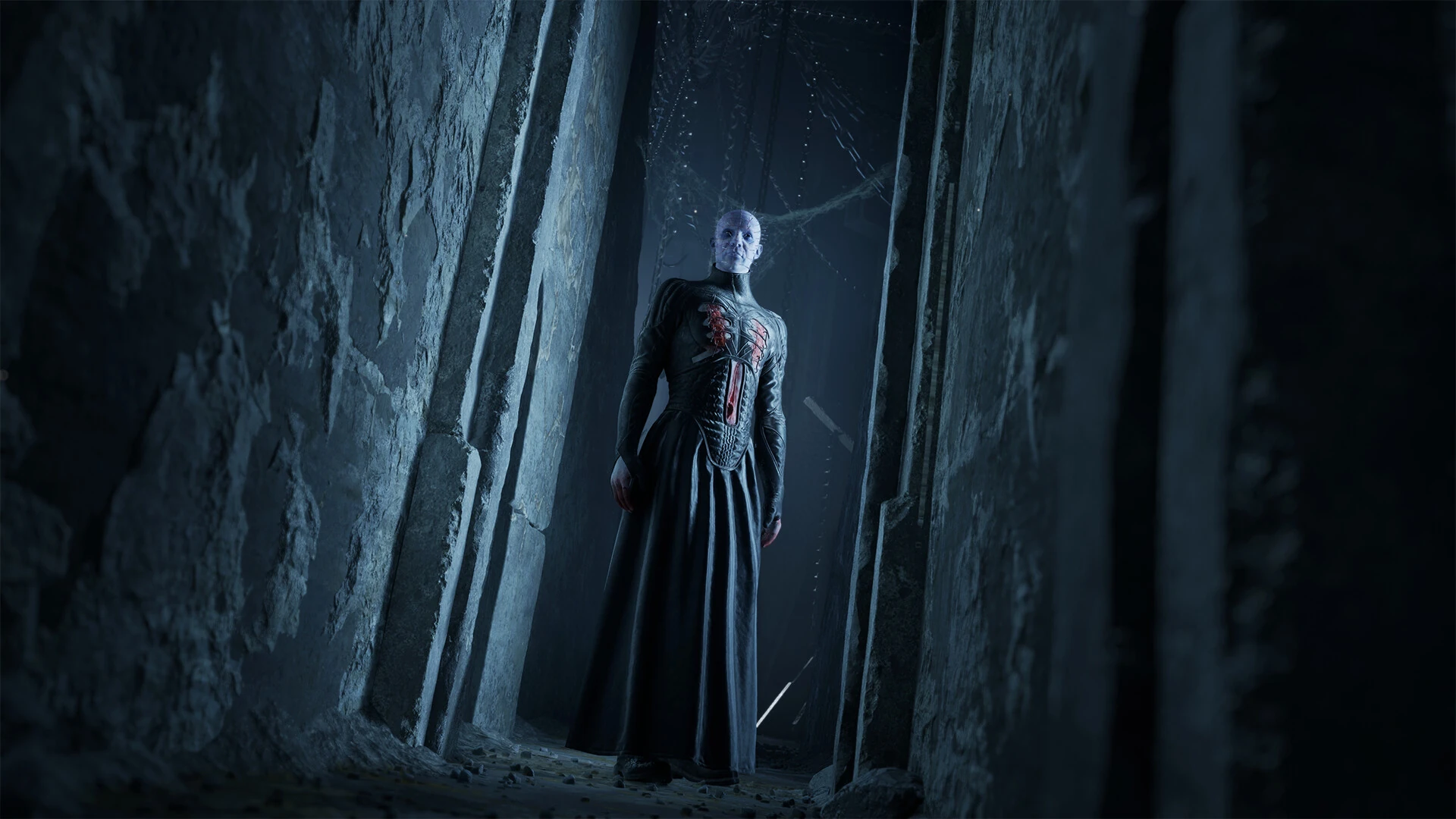 Pinhead, con la cabeza llena de clavos y túnica negra de cuero, en la boca de un pasillo estrecho de piedra