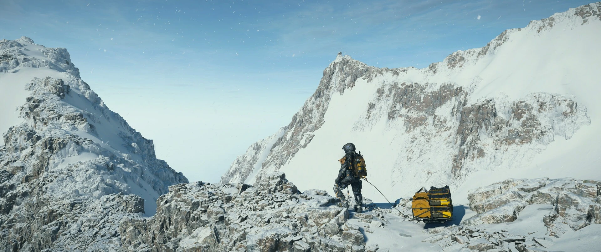 Un porteador, pequeño en el centro, junto a su carga en una cresta nevada entre dos picos