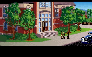 Indiana Jones de pie ante Barnett College hablando con dos hombres de traje, con el morro de un coche azul a la derecha y el texto Dr. Jones