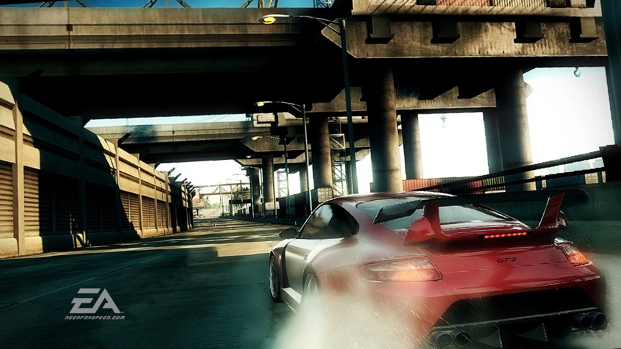 Un Porsche 911 GT2 rojo y plateado acelera bajo una autopista elevada, levantando polvo