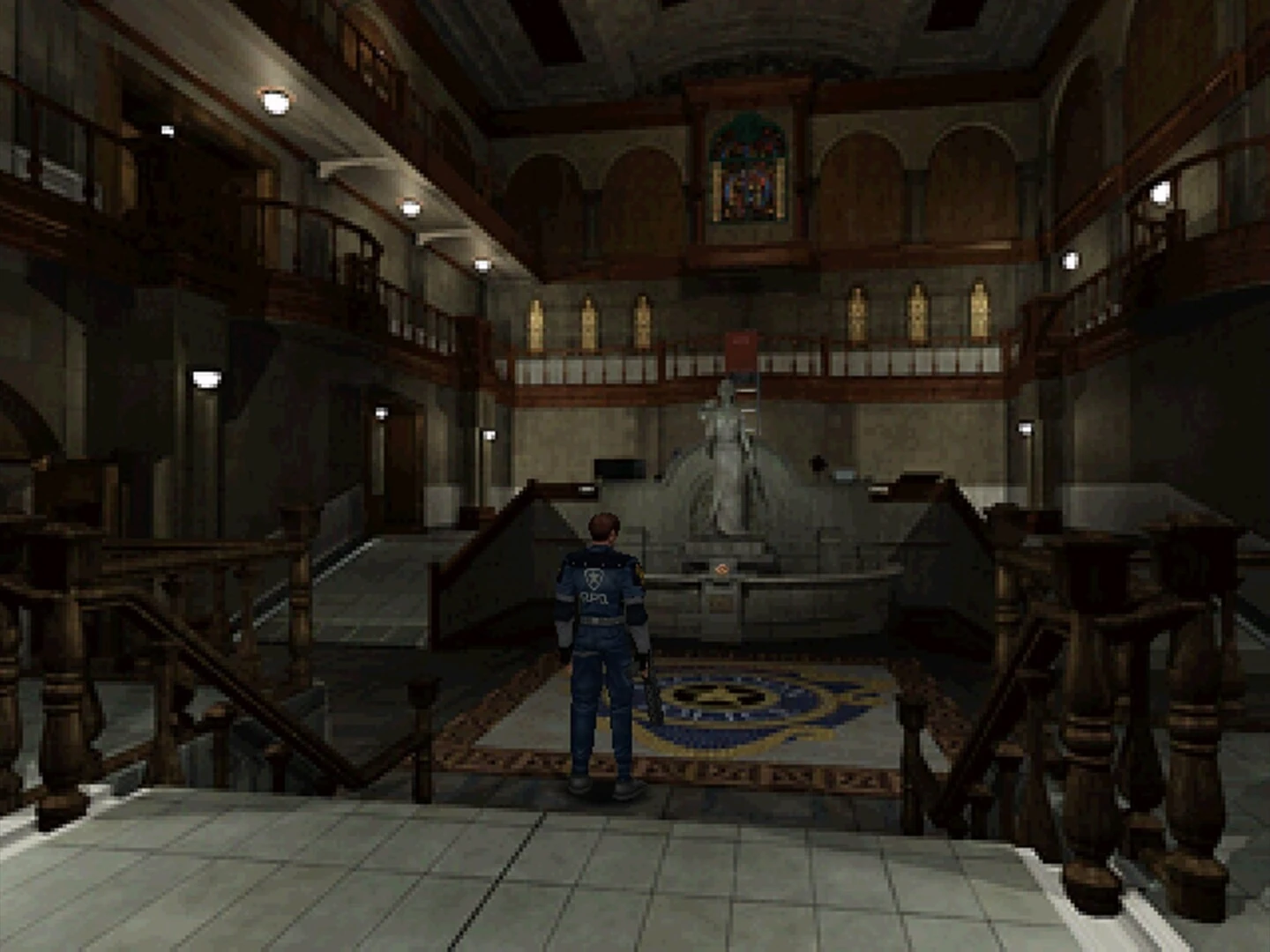 Leon, de espaldas, en el vestíbulo de la comisaría de Raccoon City, frente a la estatua central