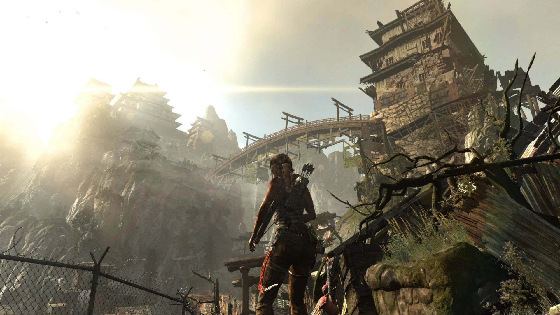 Lara Croft, con el arco a la espalda, mira un poblado de chapa y madera y un templo japonés en lo alto de un acantilado