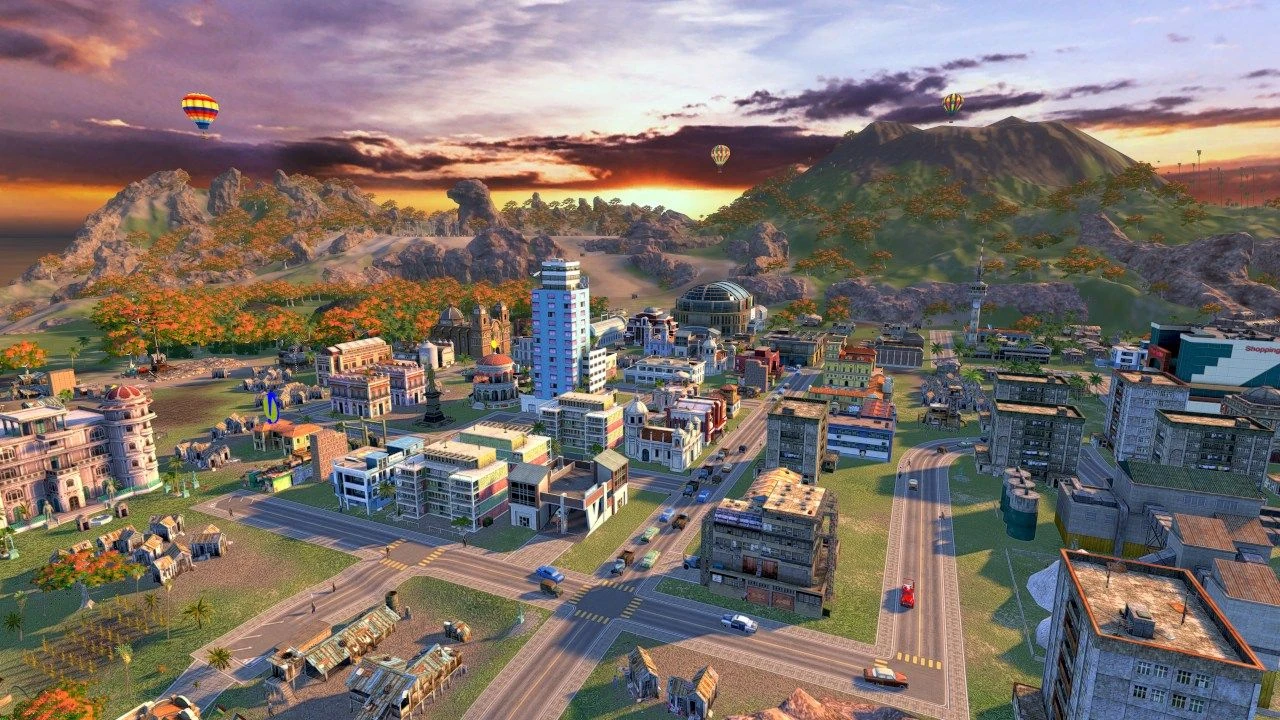 Vista aérea de una ciudad isleña al atardecer, con calles, bloques de pisos, una catedral, globos aerostáticos y montañas al fondo