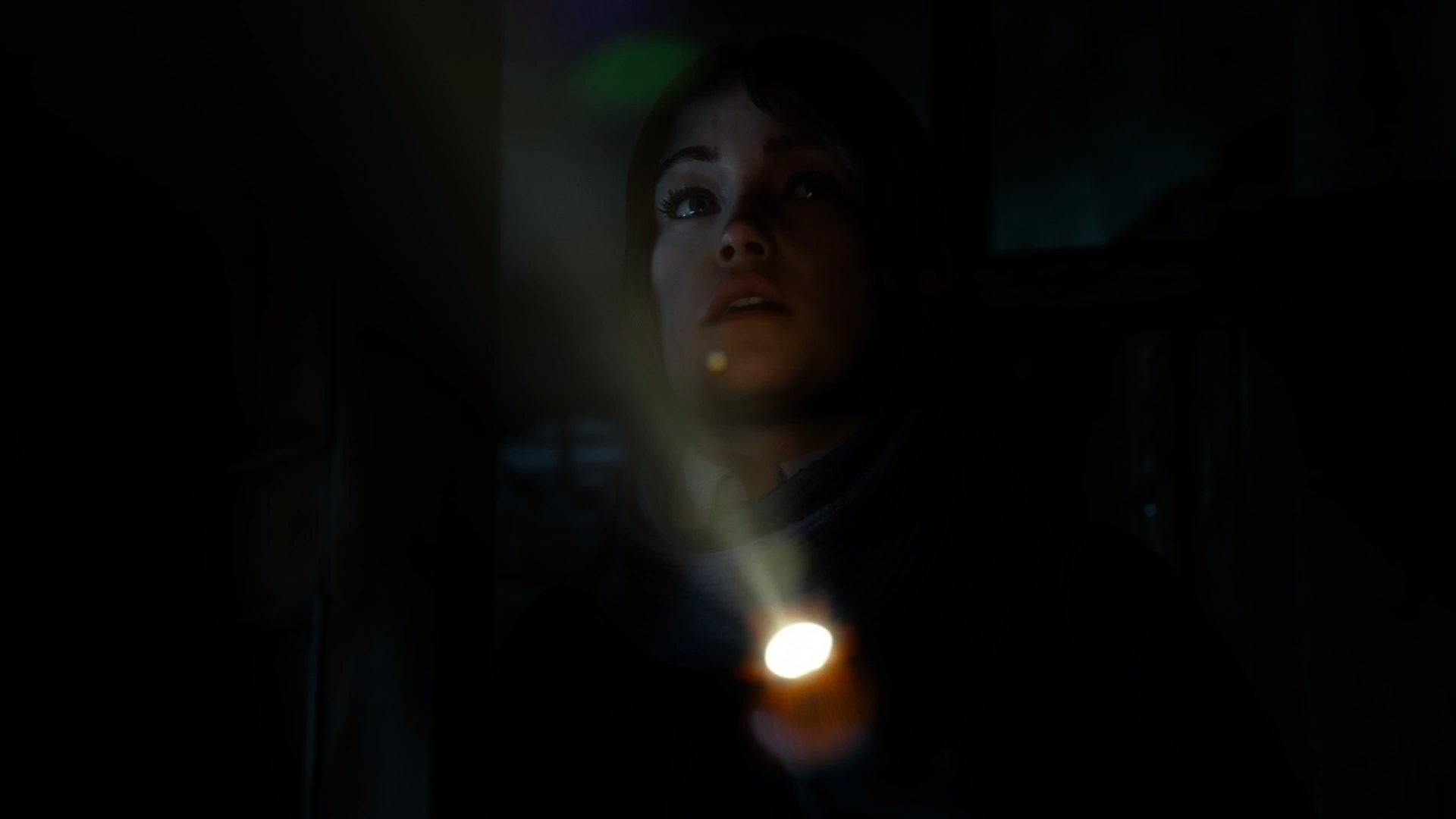 Una chica mira hacia arriba en la oscuridad, con el haz de una linterna encendida en primer plano