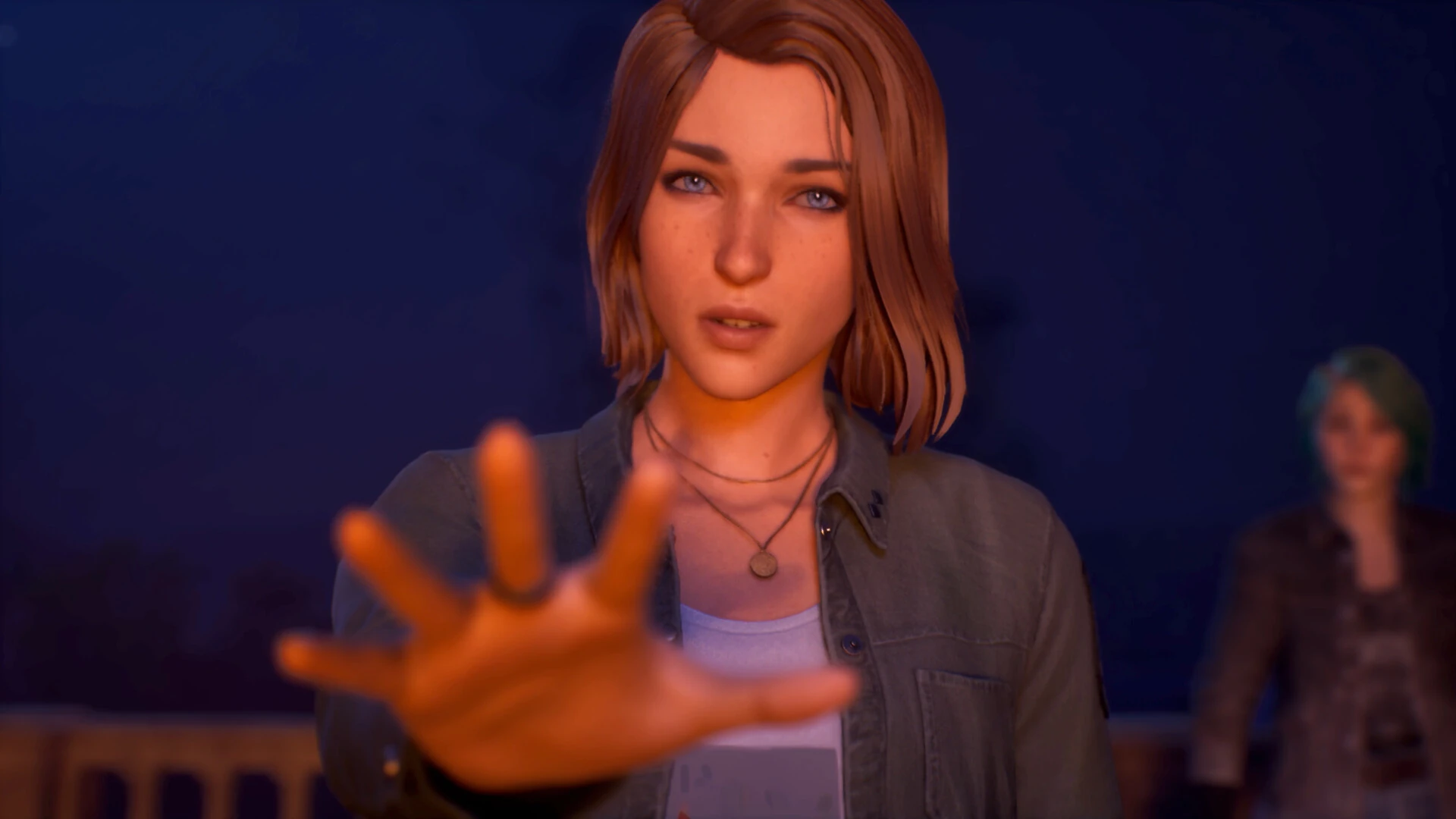 Max Caulfield, de cerca, tiende la mano hacia la cámara; Chloe Price, de pelo verde, queda desenfocada al fondo bajo una luz naranja