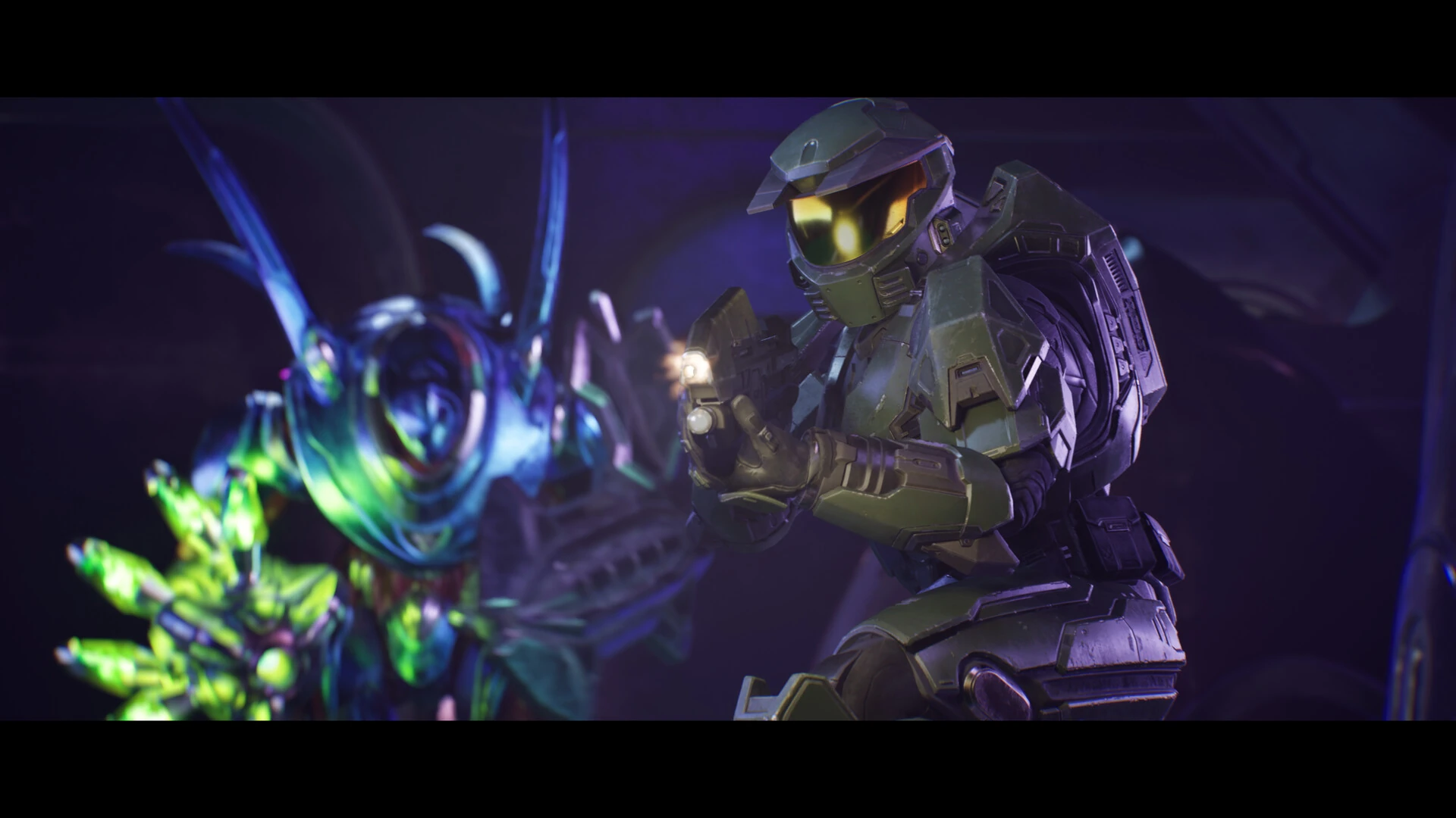 El Jefe Maestro, con la armadura verde y el visor dorado, apunta con una pistola a un alienígena azul y verde de mandíbulas abiertas